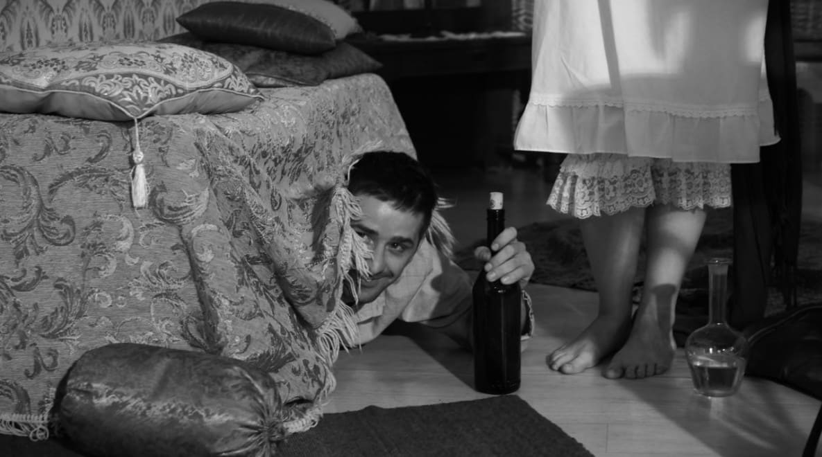 Film Take: Joyful Šmulik looks up from under his bench with bottle of wine in his hand